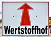 Auf einem weißen Schild ist einer roter Pfeil zu sehen, der geradeaus zeigt. Darunter steht in schwarzen Buchstaben das Wort "Wertstoffhof".