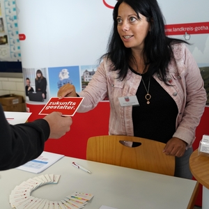 Eine Frau reicht einer Person eine rote Postkarte, auf der "Zukunftsgestalter" steht. Sie soll auf einen Ausbildungsberuf im Landratsamt hinweisen.